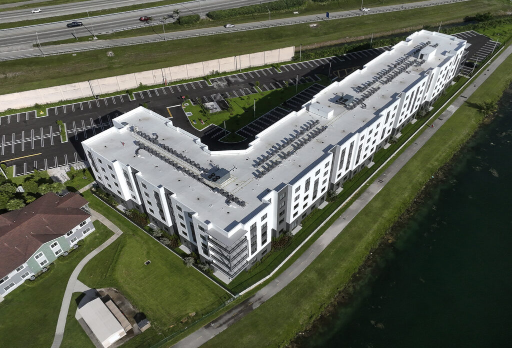 Close-up aerial view of Old Cutler Village Phase 2 luxury affordable housing showing L-shaped building design with white exterior and extensive parking in Homestead Florida